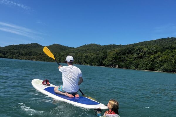Mann auf einem Stand-up-Paddle-Board, daneben ein schwimmendes Kind