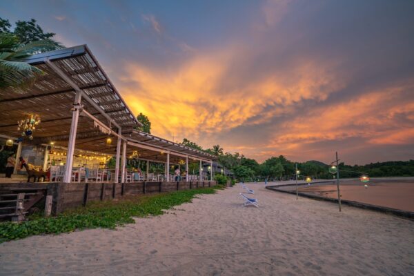 Überdachte Bar am Strand unter orange leuchtendem Abendhimmel