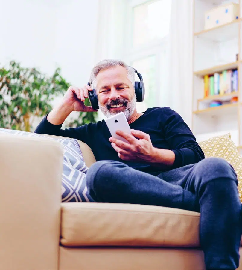 Mann mit Kopfhörern auf dem Sofa hört einen Podcast